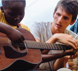A Music Volunteer teaching a boy how to play the guitar