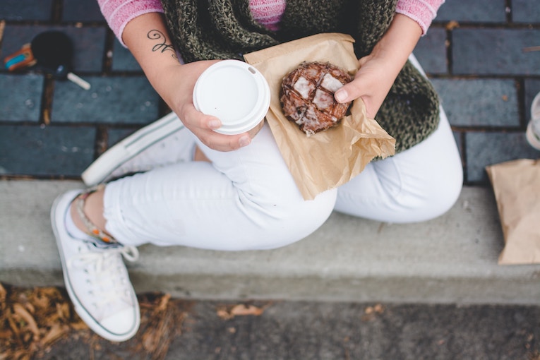 person sitting on ground and holding coffee and pastry