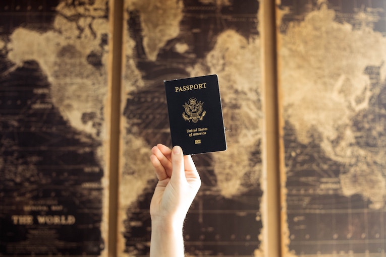 hand holding up passport in front of map of the world