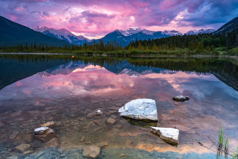 water near trees and mountain under purple sky