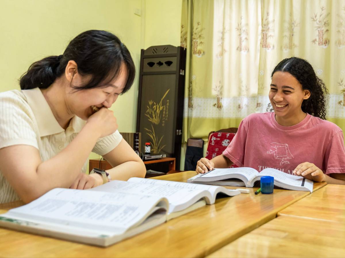 A Chinese teacher and student laugh together over open textbooks during a Mandarin lesson at the CLI Center in Guilin.
