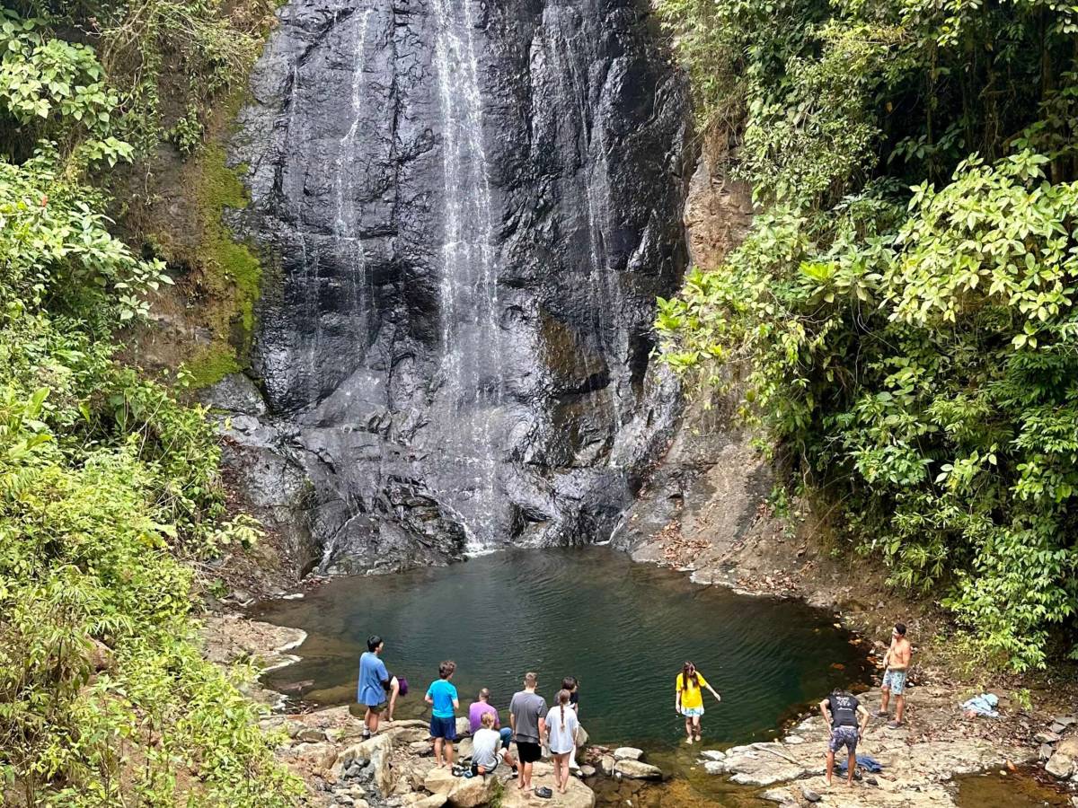 A distance shot of a waterfall, with a group of people gathered at the base.