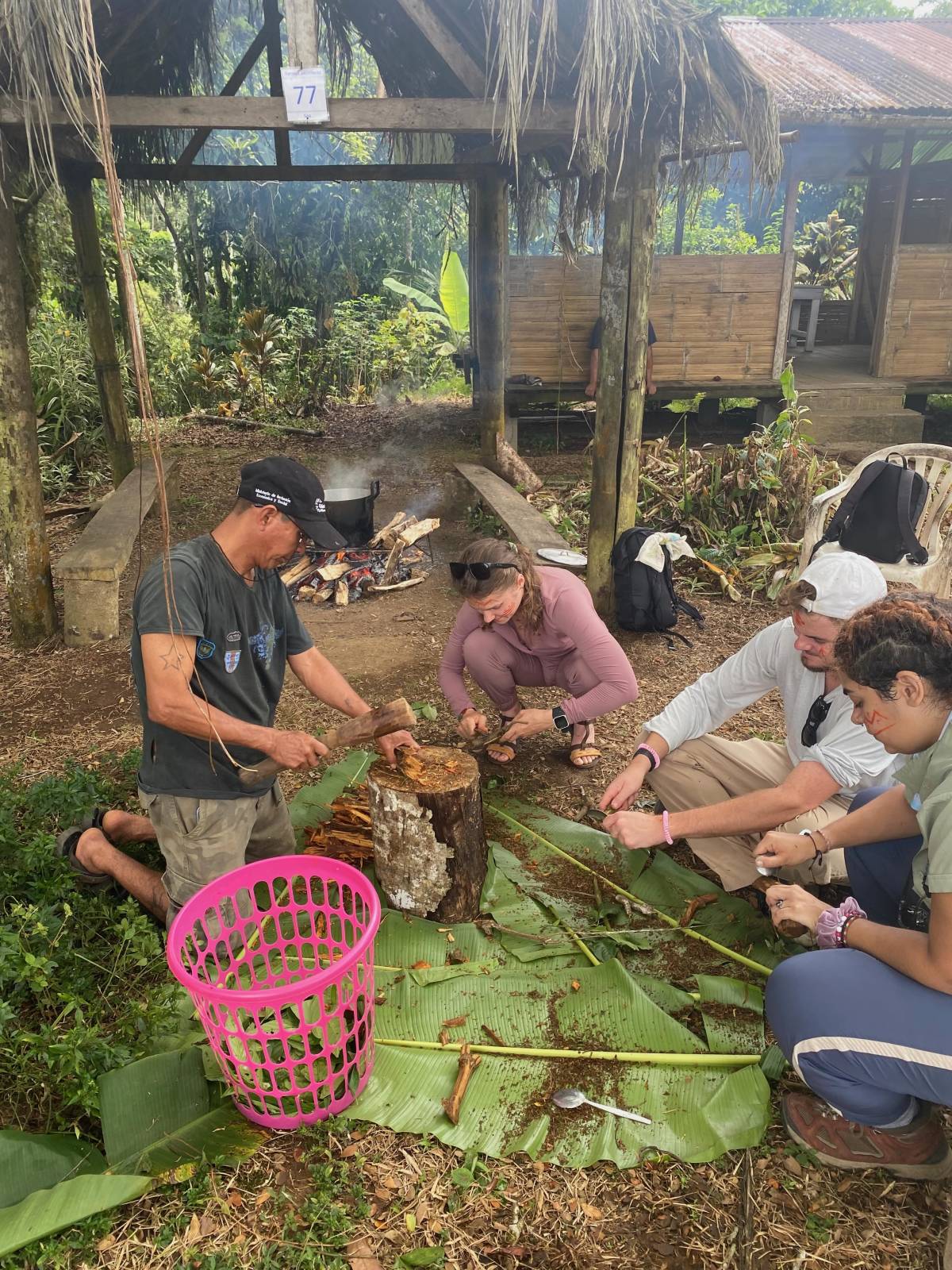 A group gather around the ground, peeling and processing pieces of vine in natural setting.