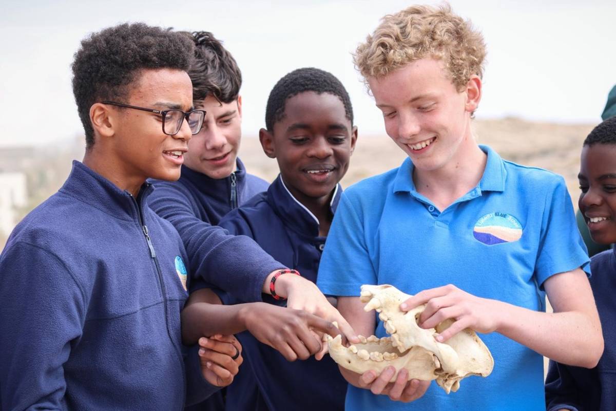 A group of Lüderitz Blue School students in uniform examining a specimen together outdoors during an Ocean Day visit from the Brown Hyena Research Project.