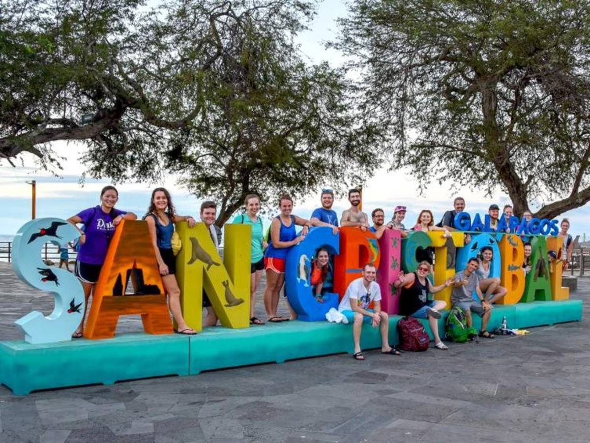 A group of students stands by the San Cristobal Galapagos sign.