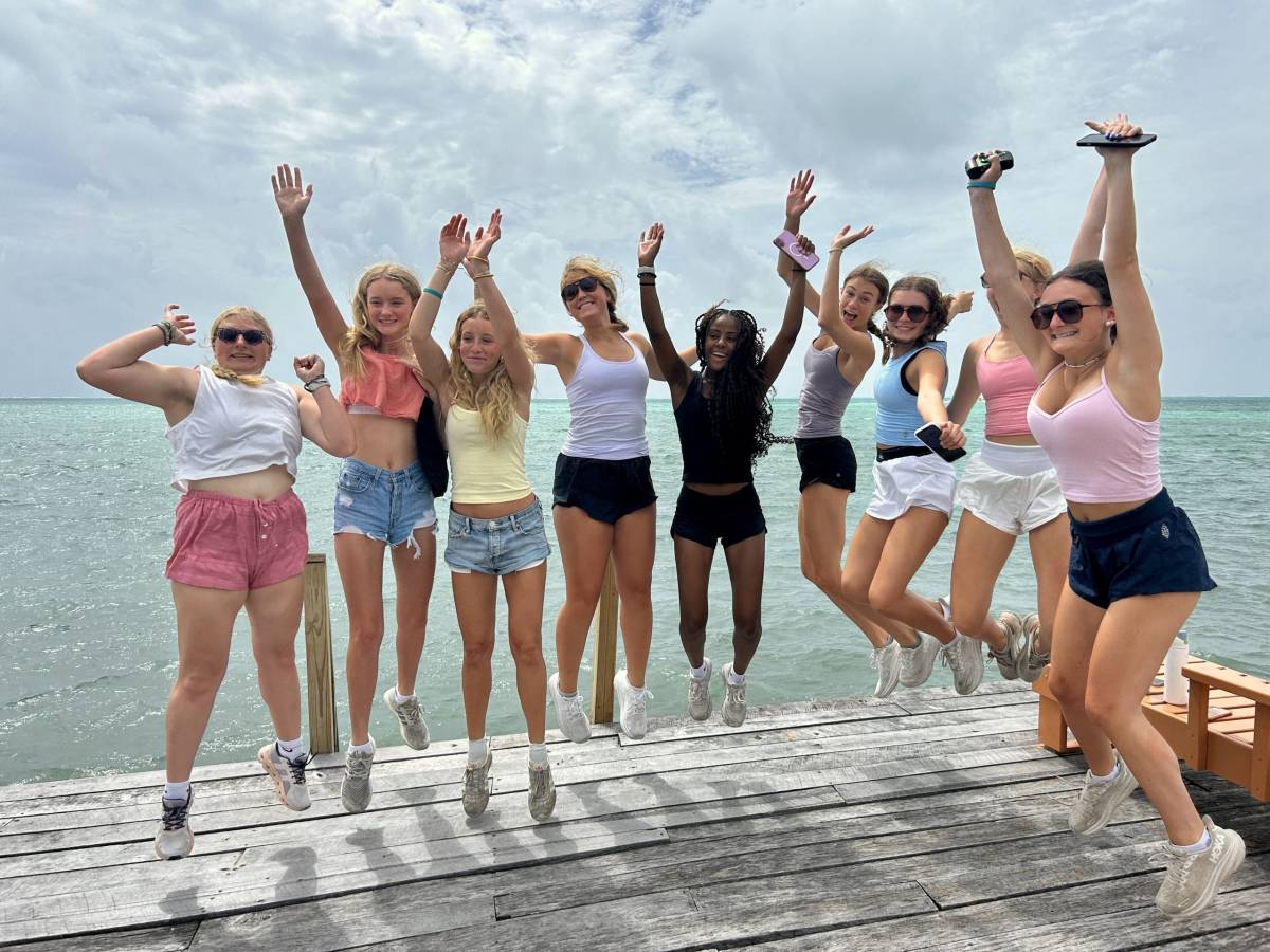 A group of teens jump on a boardwalk next to the ocean in Belize