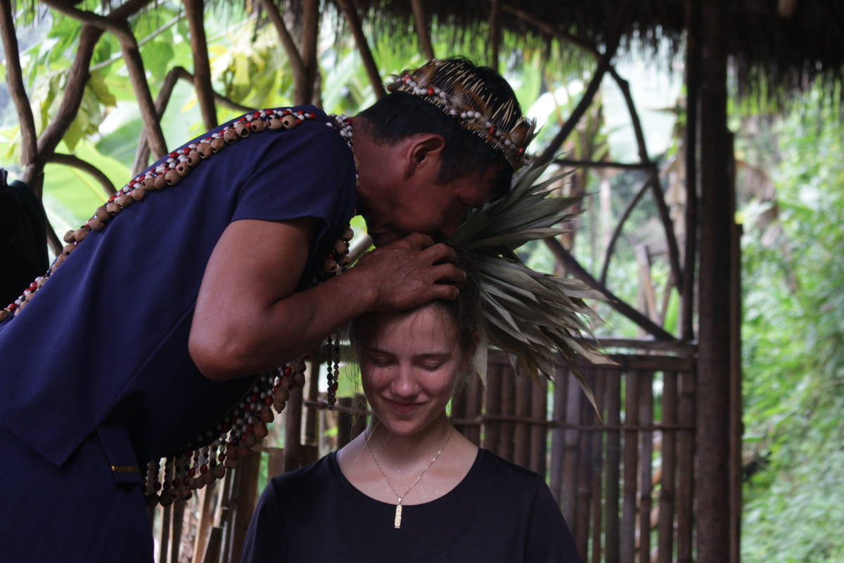 A man in traditional clothing blows onto the head of a visitor, in a type of cleansing ceremony.