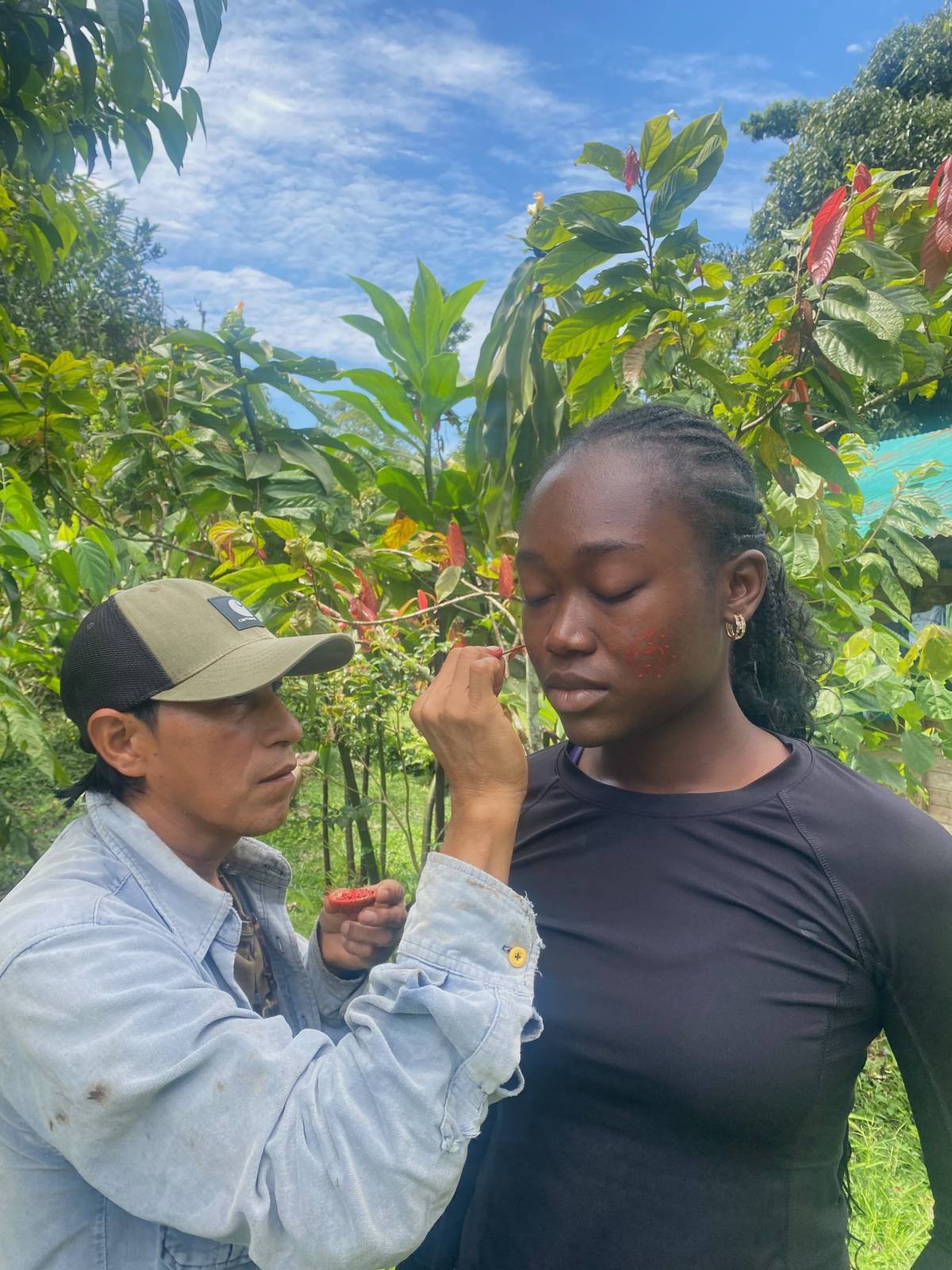 A man paints a woman's face with achiote, a local product, in a jungle setting.