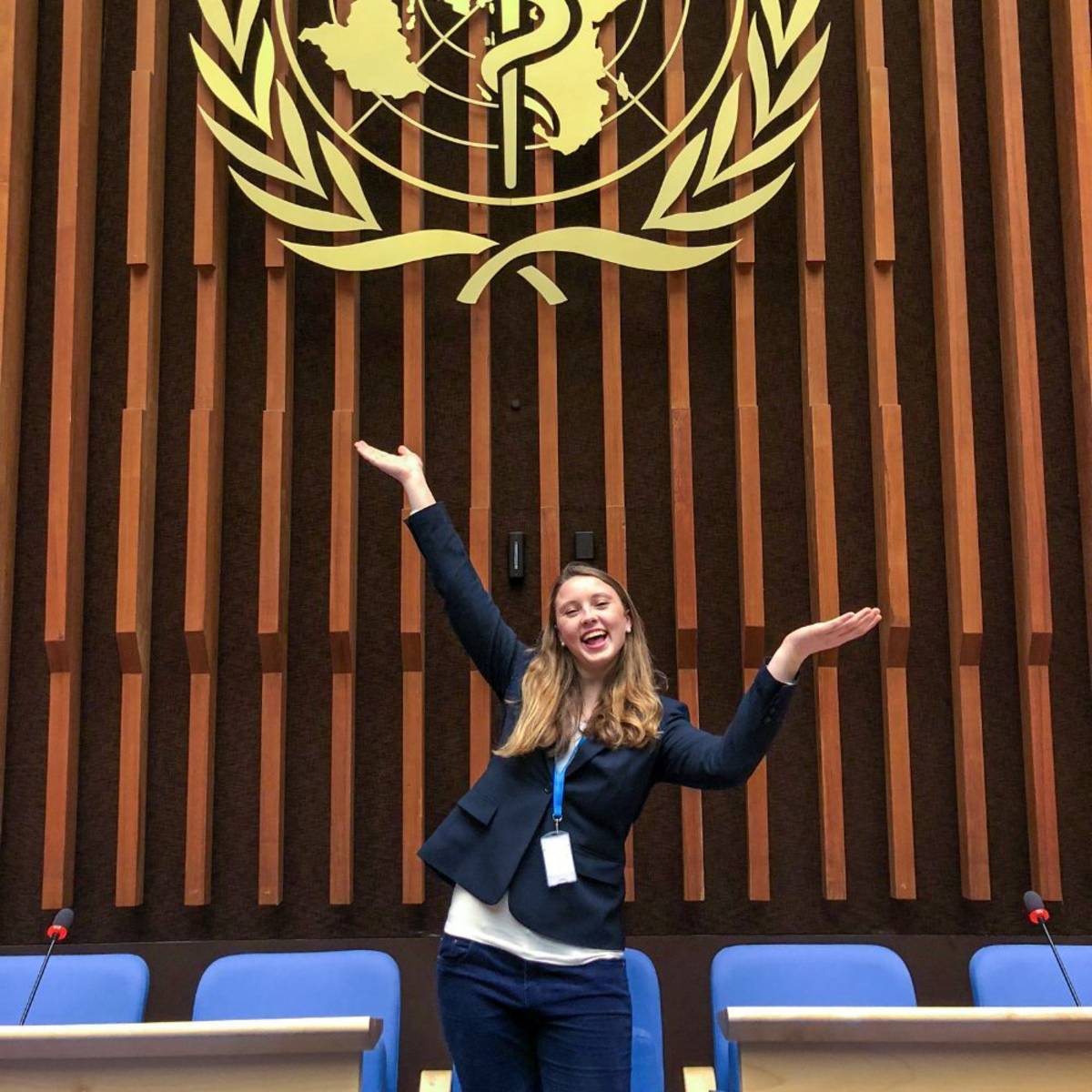 A student posing with arms outstretched under the World Health Organization logo