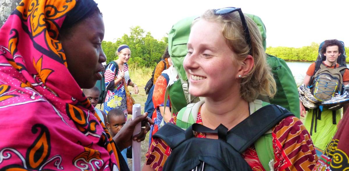 A student smiling at a Kenyan women, other students and Kenyan children in the background