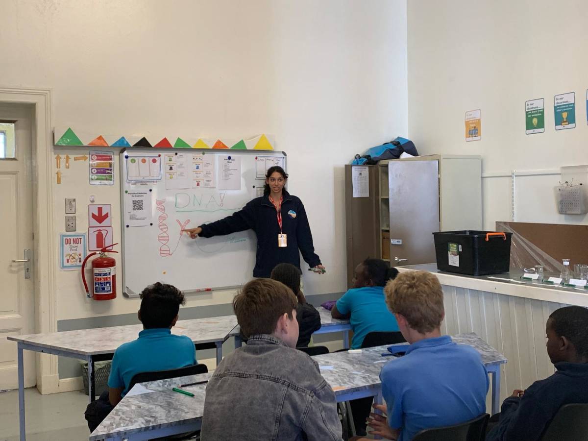 A teaching intern pointing to a DNA diagram on a whiteboard while secondary school students follow along in class at Lüderitz Blue School.