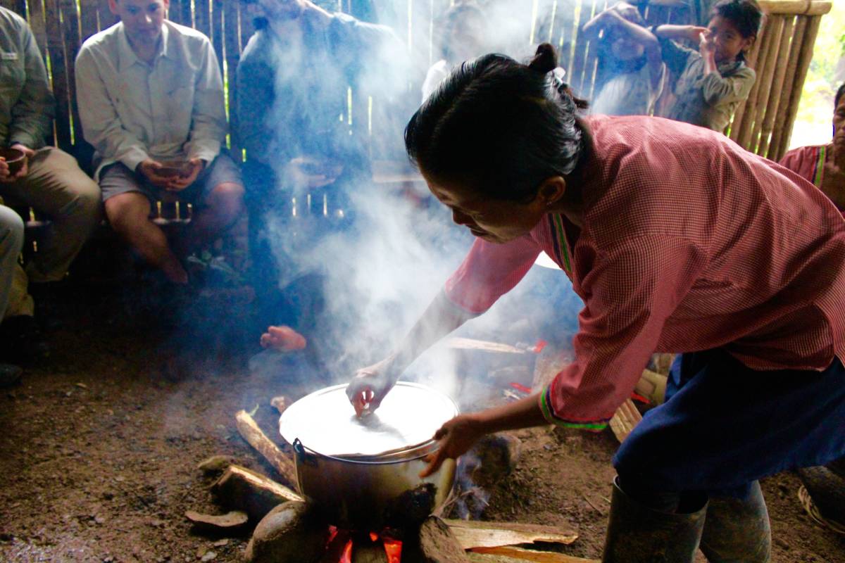 A woman leans over a steaming pot cooking on a woodfire.
