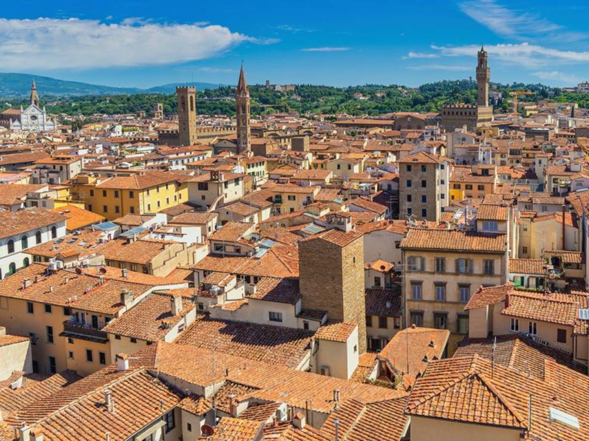 Aerial view of Florence, Italy with iconic red rooftops, historic buildings, and the Arno River winding through the city.