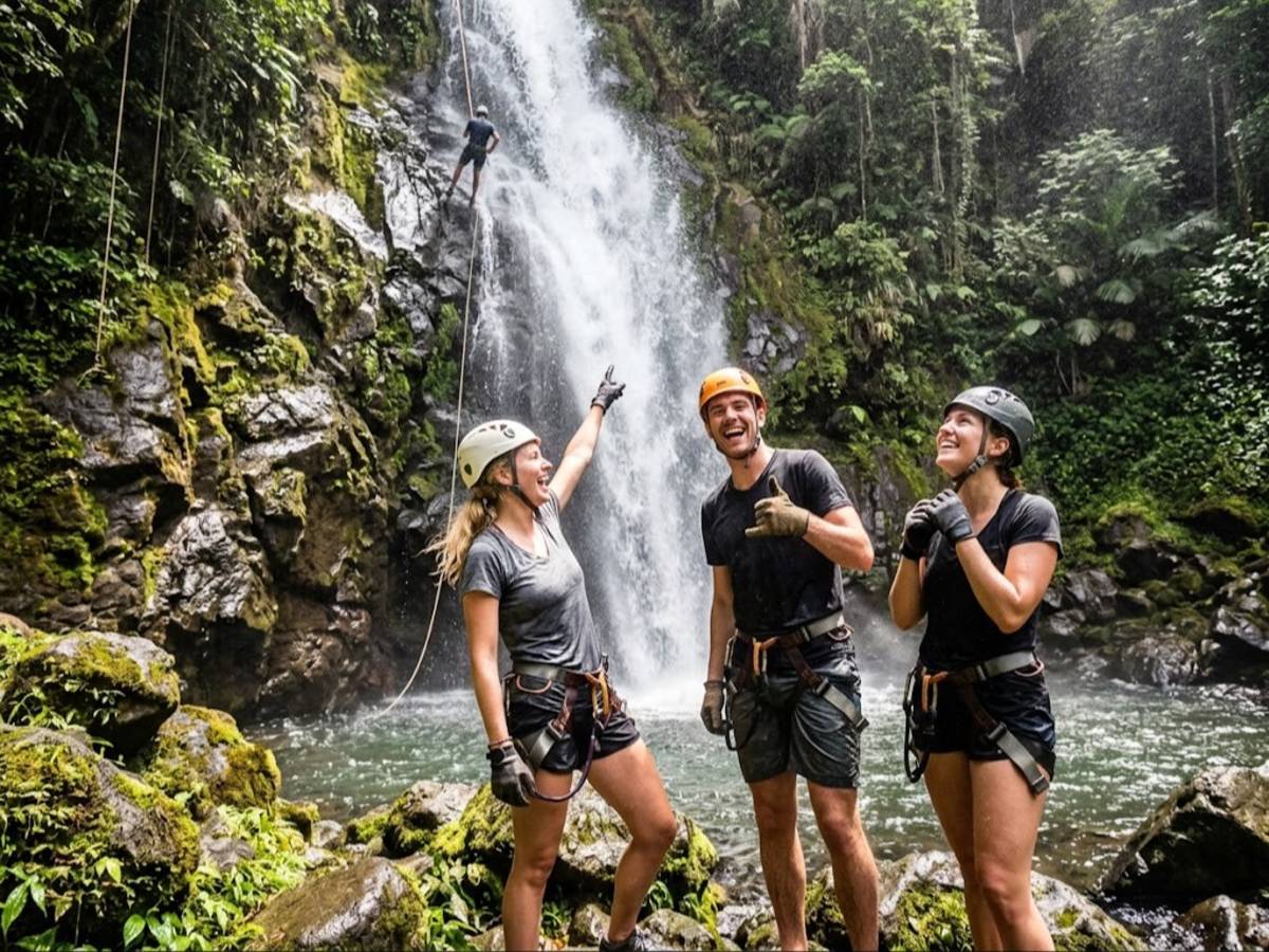 Alt text: Adventurers smiling near jungle waterfall after rappelling down rocks