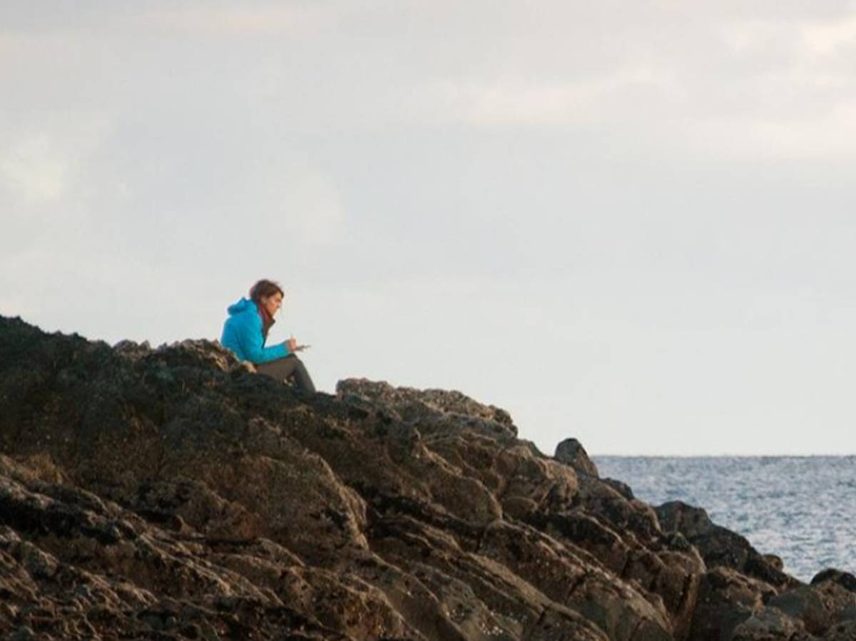 dublin student sitting on a rocky shore by the sea writing