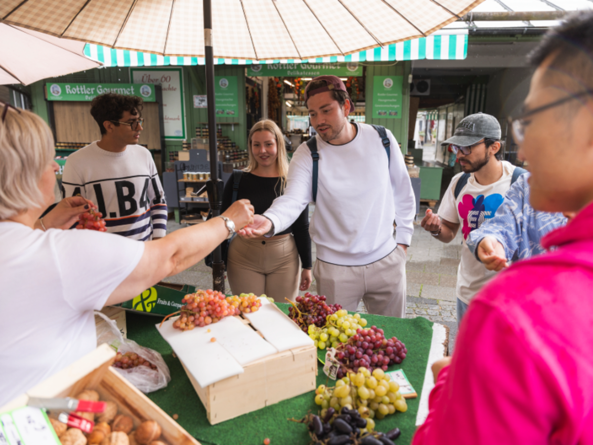 EF Munich students explore a local market, sampling fresh grapes and practicing German while interacting with vendors.