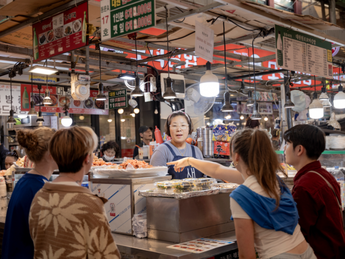 EF students ordering food from a vendor at a traditional market in Seoul, surrounded by colorful signs and dishes.