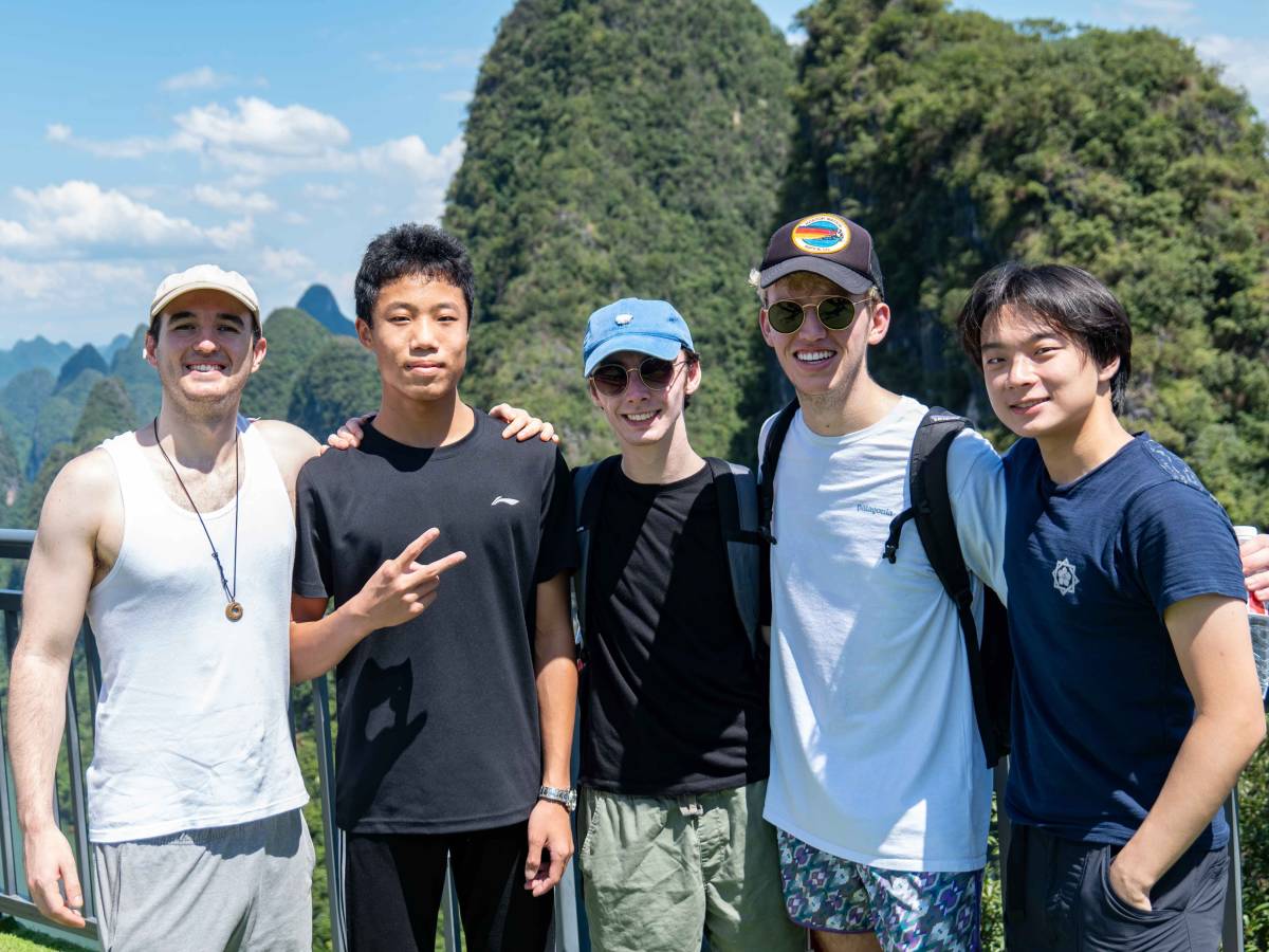 Five young men pose arm in arm at a scenic overlook above the Li River, with green karst mountains rising behind them.