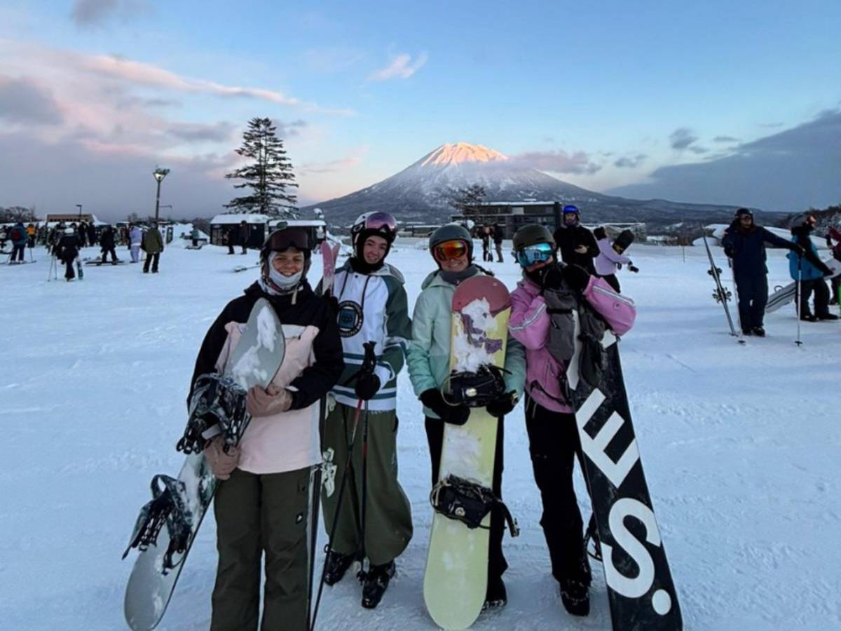 Four people standing with snowboards on a snowy mountain