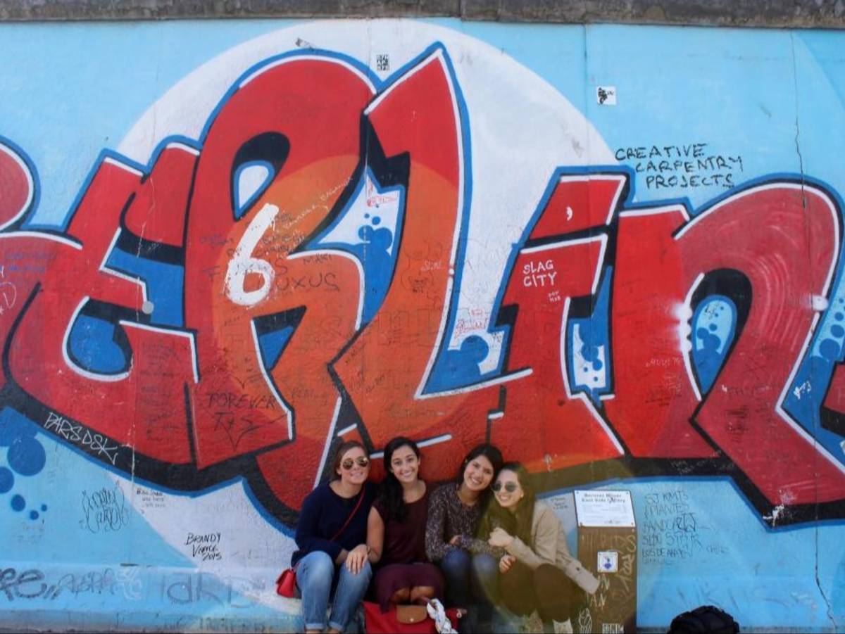 Four students sit in front of a blue wall that reads Berlin in red graffiti.