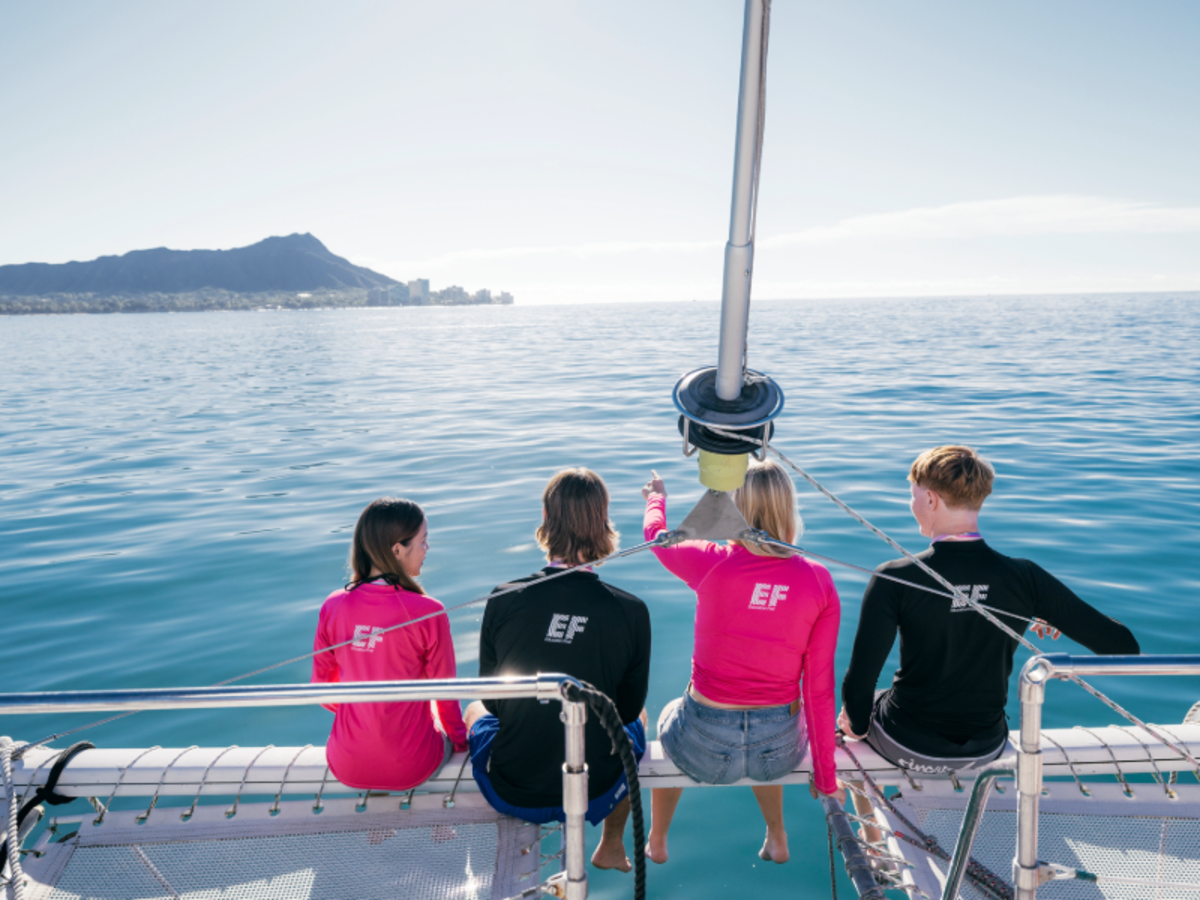 Group of EF students sitting on the edge of a catamaran, looking out over the calm ocean waters near Playa Tamarindo, Costa Rica.