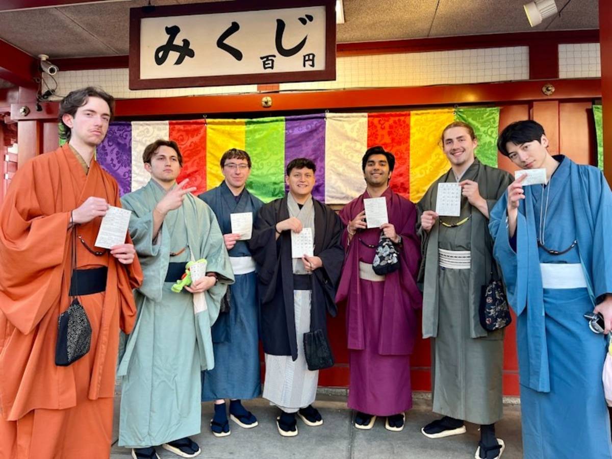 Seven students standing in colorful kimonos showing their papers received during a temple visit