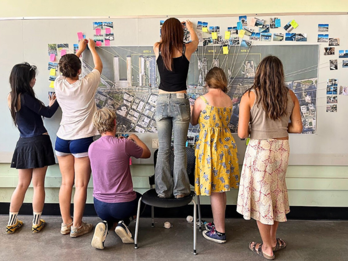 Six students facing the wall pinning up details into a large photo printout