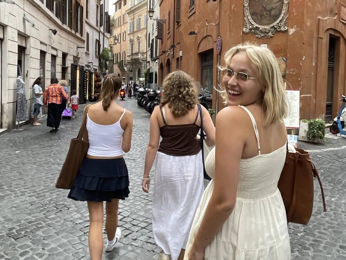 Student looking back and smiling while walking in Rome with friends on cobblestone streets.