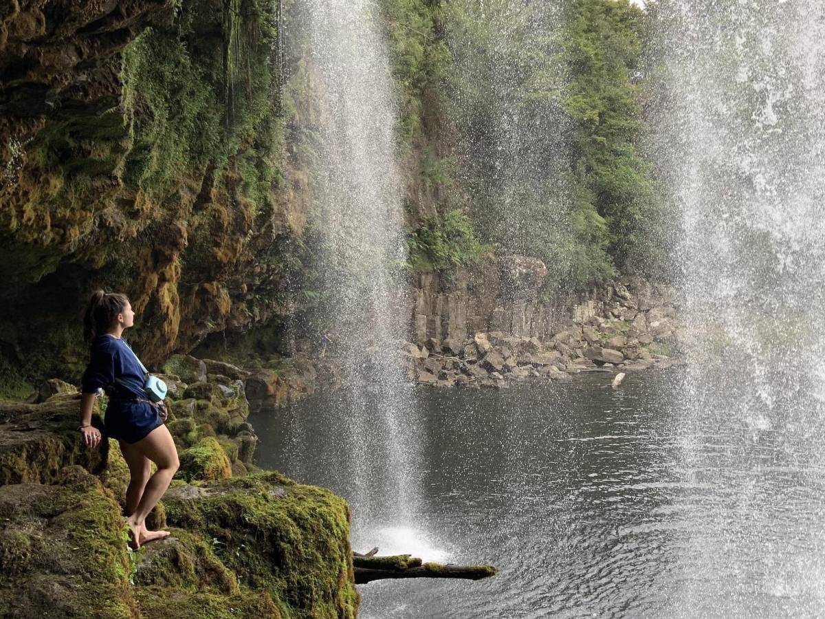 student standing beneath a waterfall and body of water