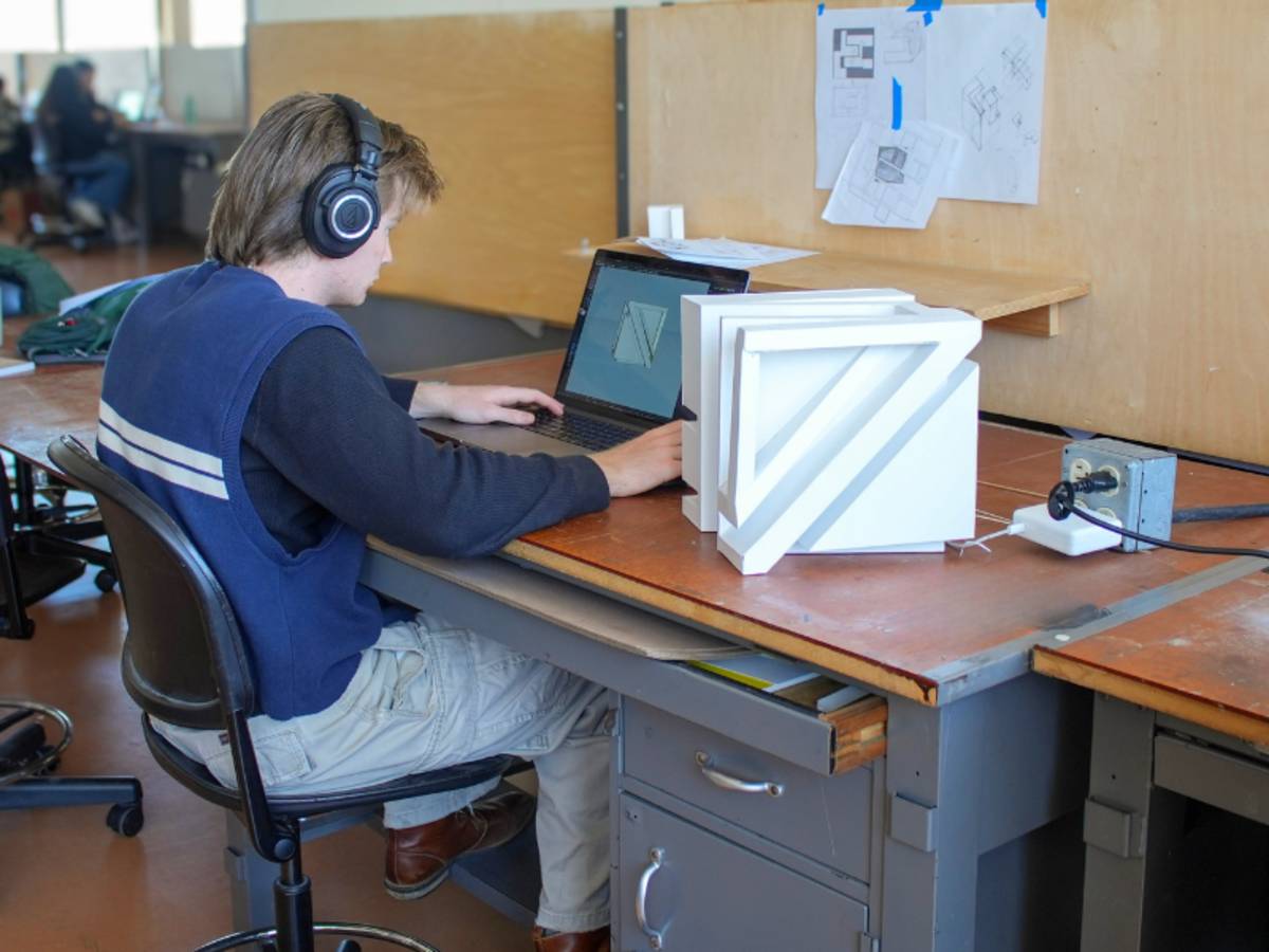 Student with headphones working on laptop with paper model on table