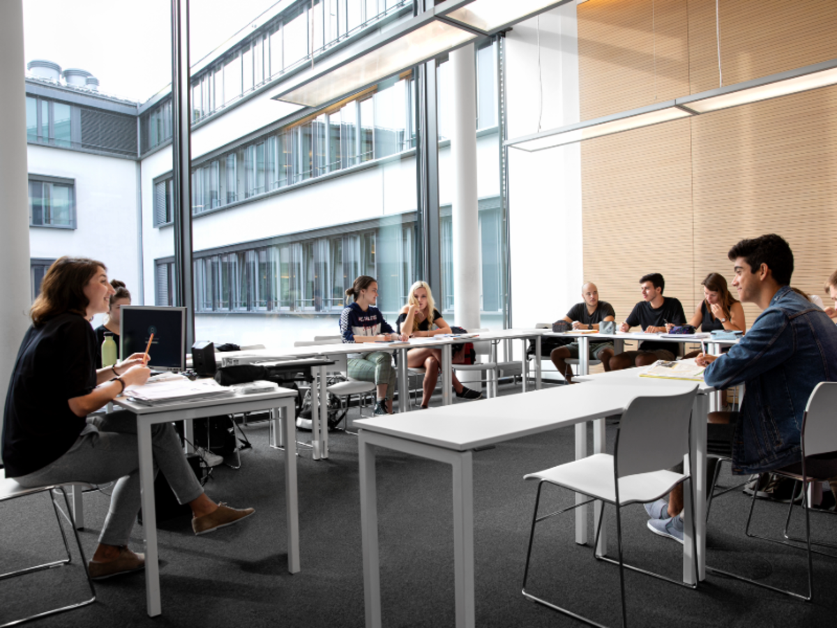 Students attend a German language class at EF Munich, seated in a bright modern classroom with large windows and natural light.