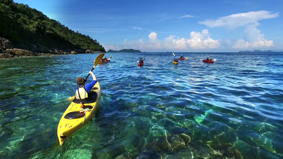 Students ocean kayak through clear blue water with an island in the background