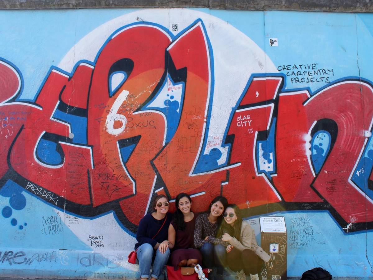Students pose in front of Berlin wall art.