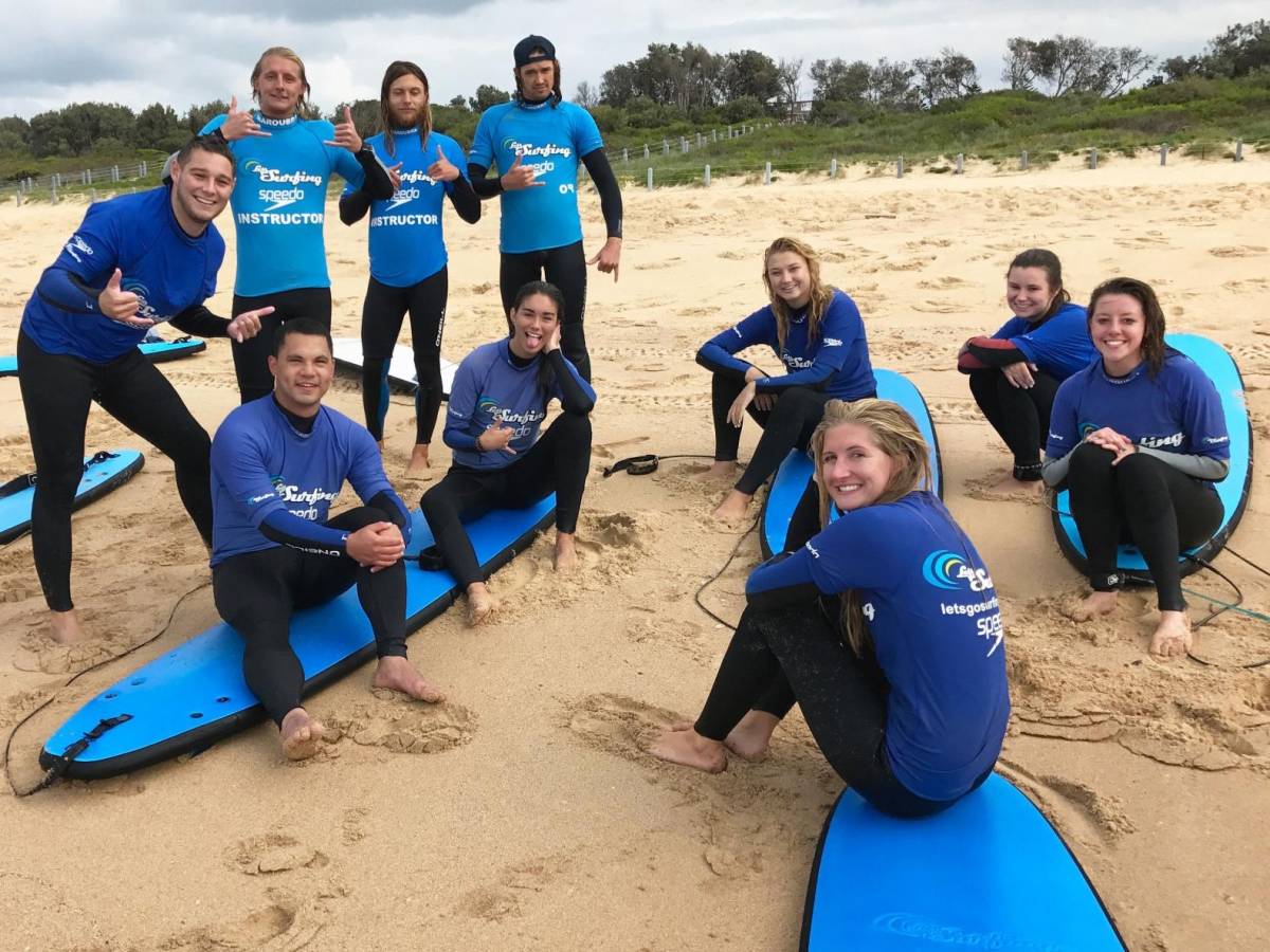 students sitting on surf boards on the beach during surf lessons