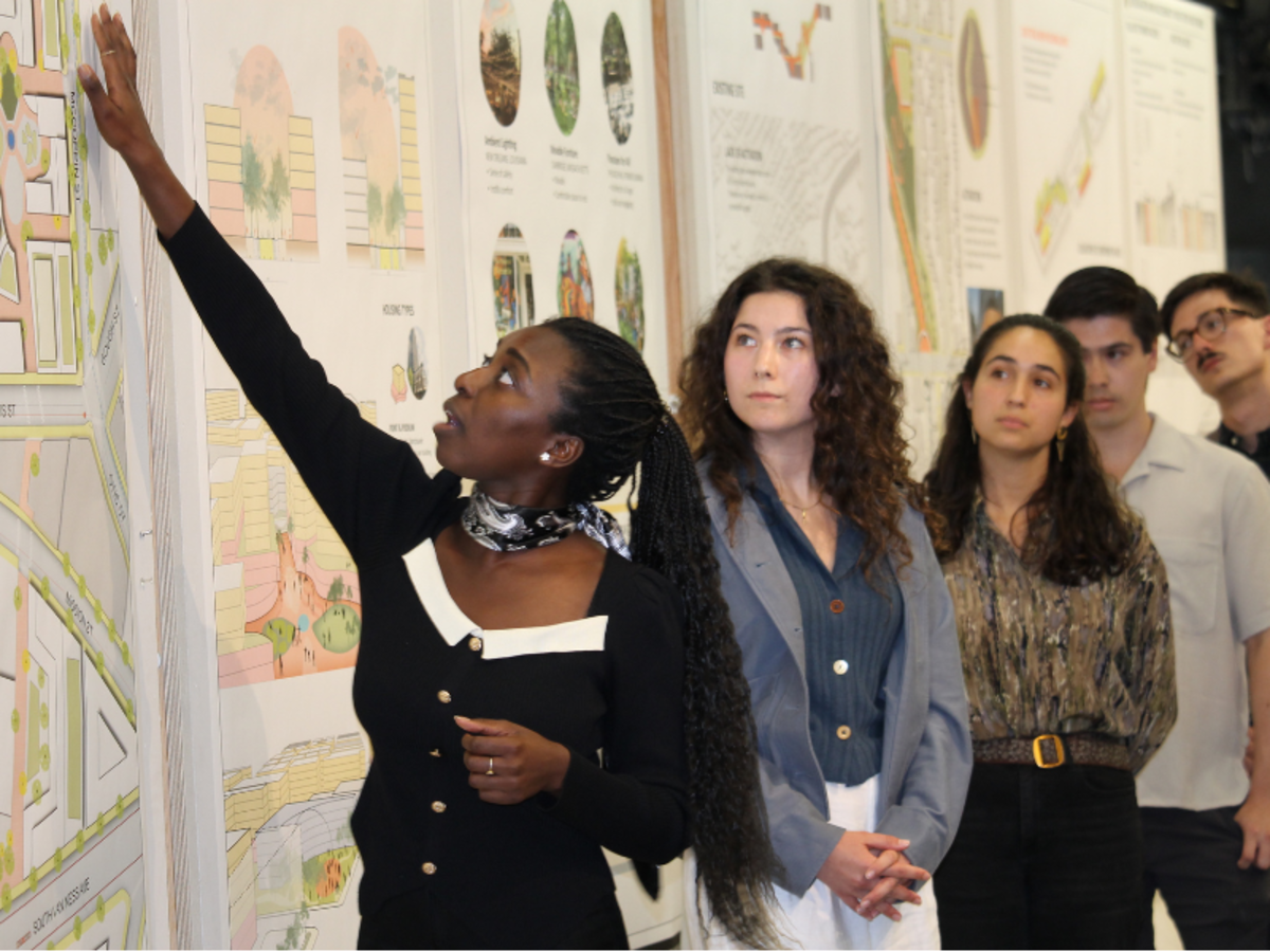 Students standing in front of their pin-ups, one is explaining