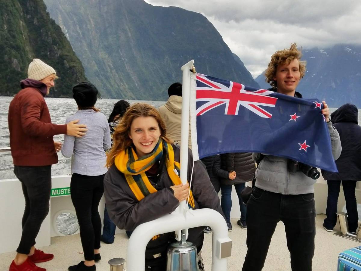 students with the New Zealand flag while on a boat cruise in Milford Sound, surounded by clouds and moutains