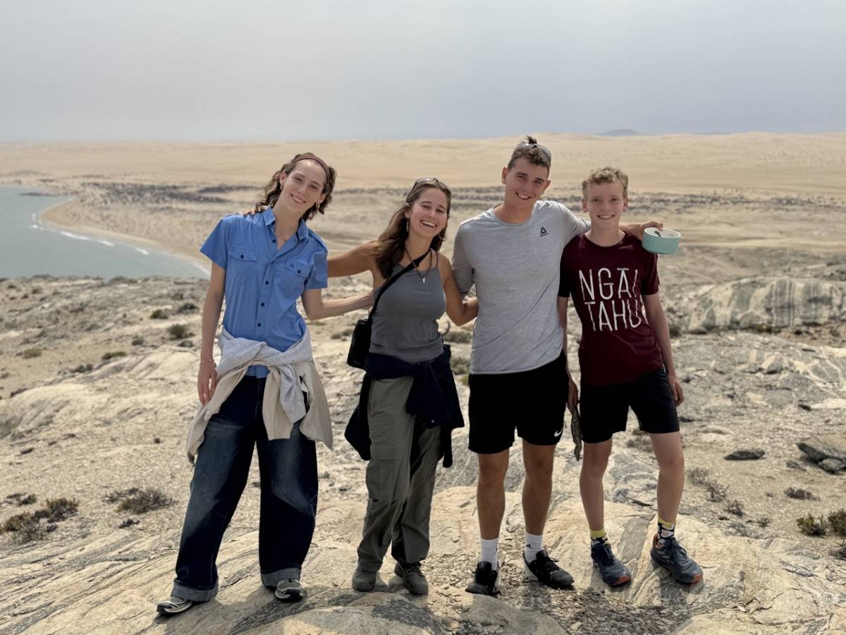 Three interns and a students smiling together on a clifftop overlooking the dramatic coastline above Agate Beach in Lüderitz, Namibia.