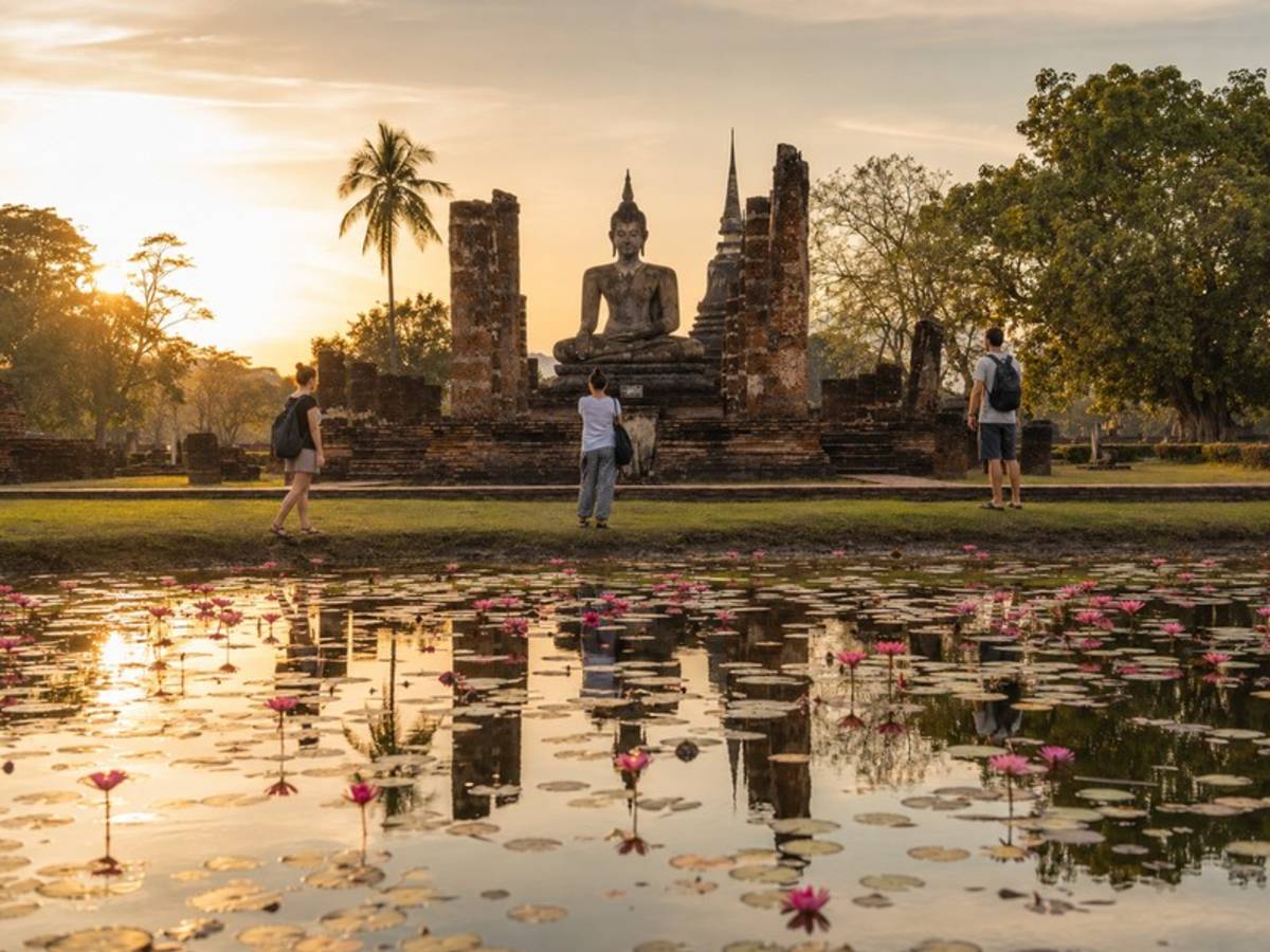 Travellers visiting an ancient Thai temple beside a lotus pond