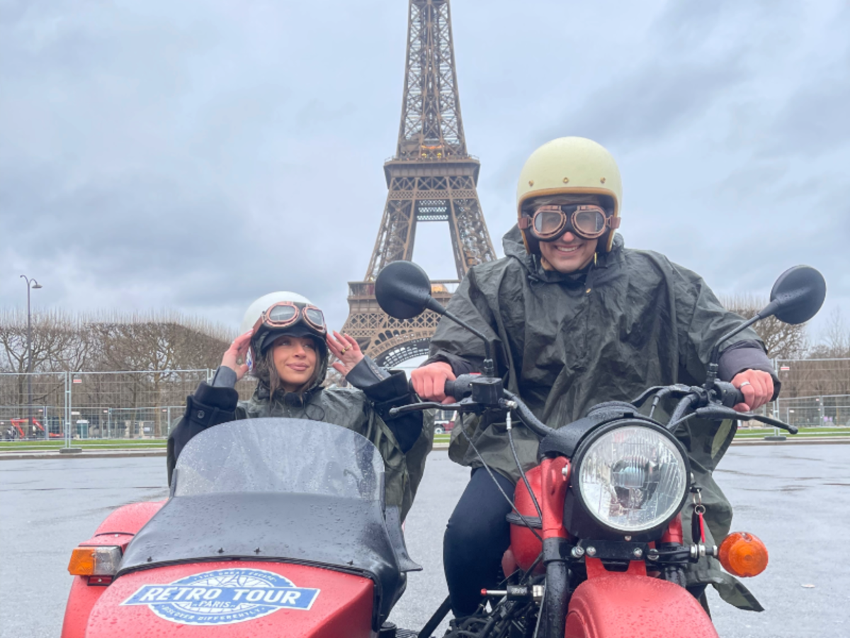 Two EF Gap Year students on a retro motorcycle and sidecar tour in Paris, smiling in front of the Eiffel Tower on a rainy day.