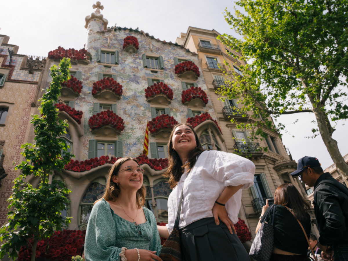 Two EF Gap Year students smiling outside Casa Batlló in Barcelona, surrounded by Gaudí’s colorful architecture and festive decorations.