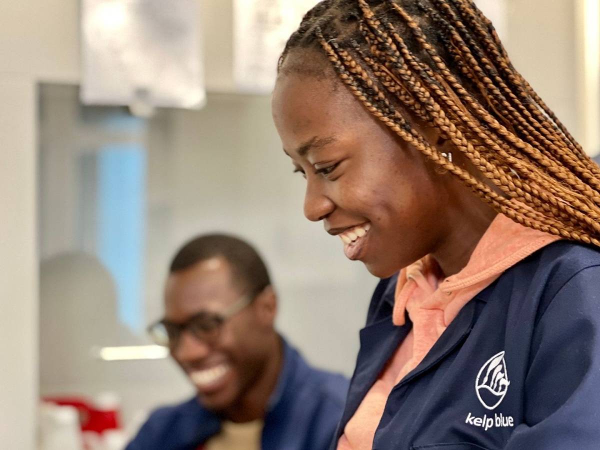 Two Kelp Blue team members laugh together in the office, one wearing a Kelp Blue hoodie.