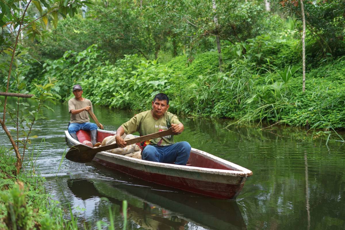 Two men row canoe through slow moving river surrounded by greenery.
