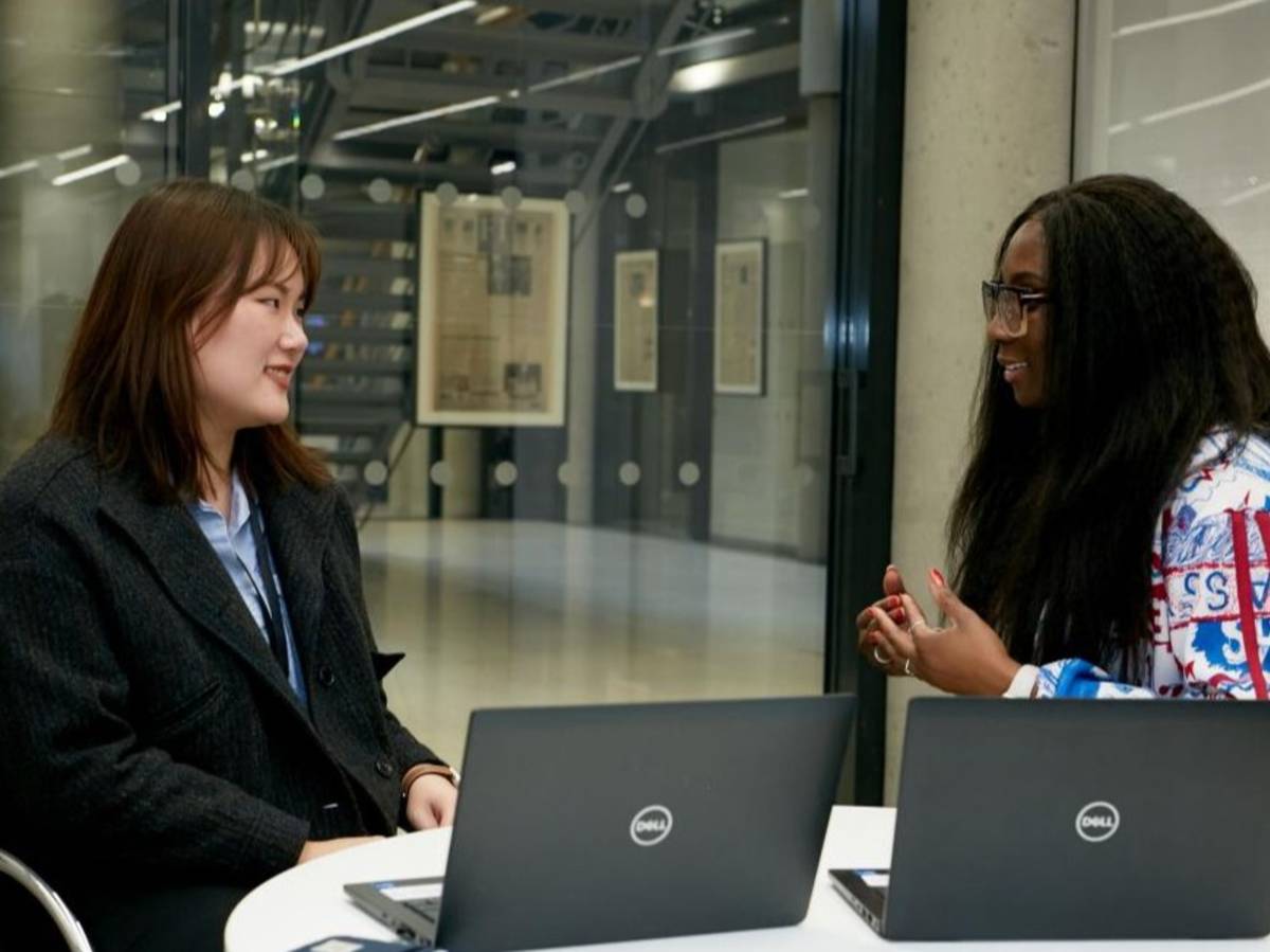 Two people seated at a table with laptops in a modern office space.
