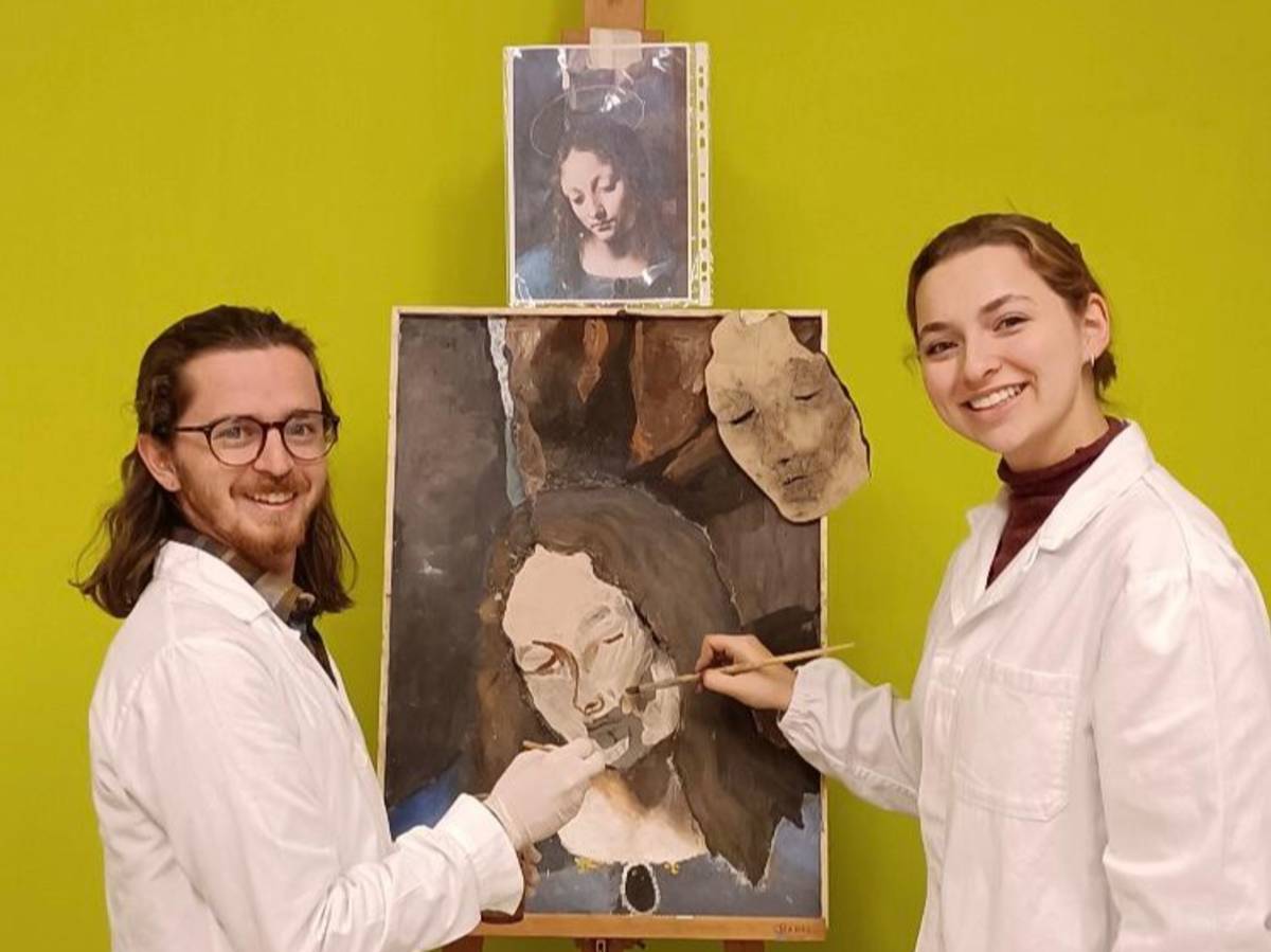 Two students in lab coats smiling in front of a fresco they are working on.