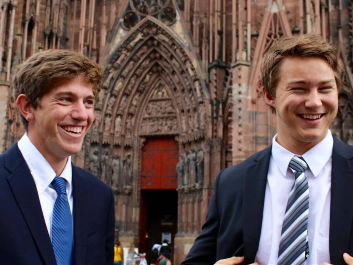 Two students in suits smile in front of the cathedral in Brussels, Belgium.