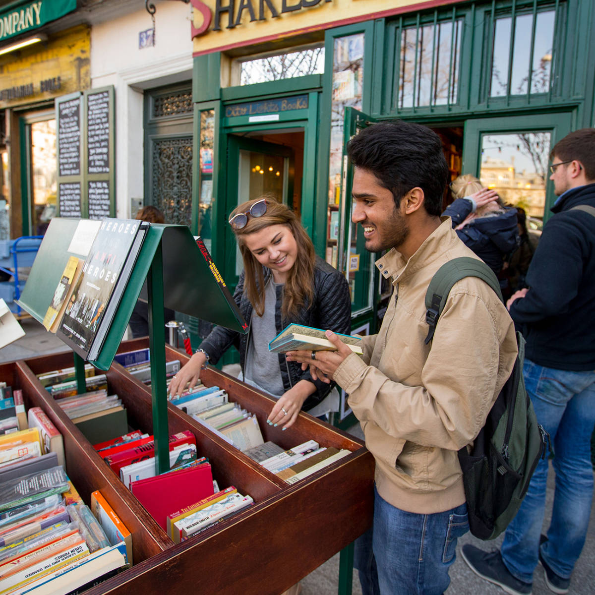 Two students smiling while book shopping outdoors.