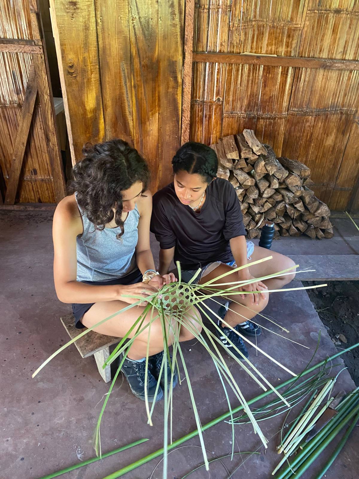 Two women weave a basket.