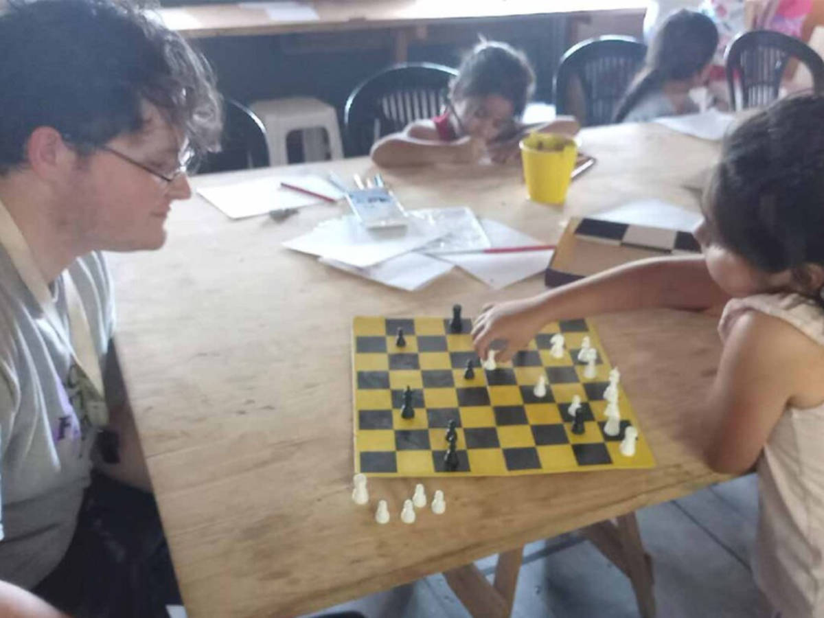 Volunteer from Mondify's human rights program playing chess with a child in a community space.