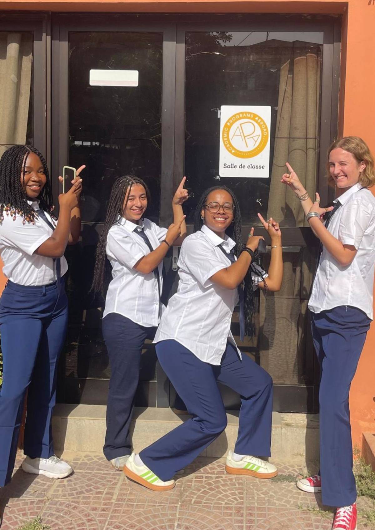 4 students point towards the APA Dakar office sign at ISM in Senegal.