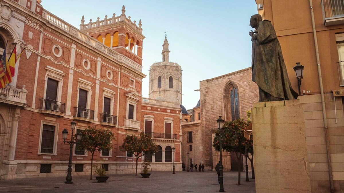 A city square surrounded by tall stone buildings, with a statue